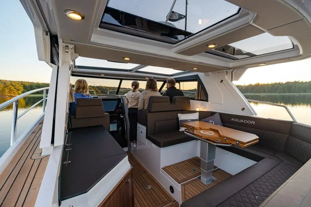 Interior of an Aquador boat with four people enjoying the view, featuring comfortable seating and a timber table.
